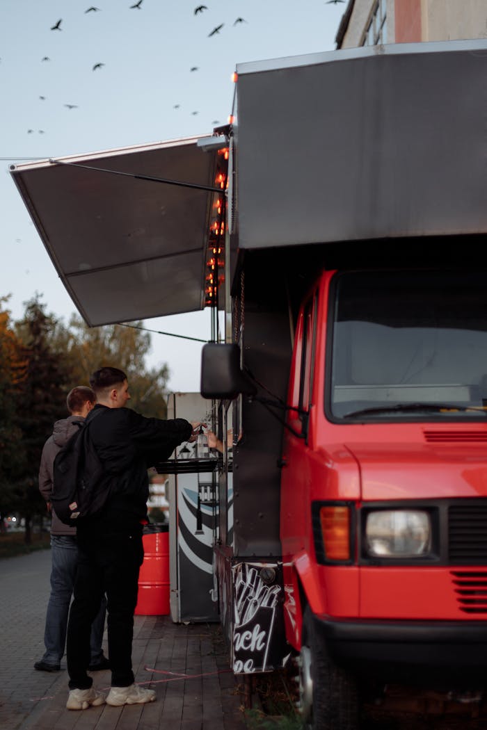 Two men ordering from a vibrant red food truck on a city street.