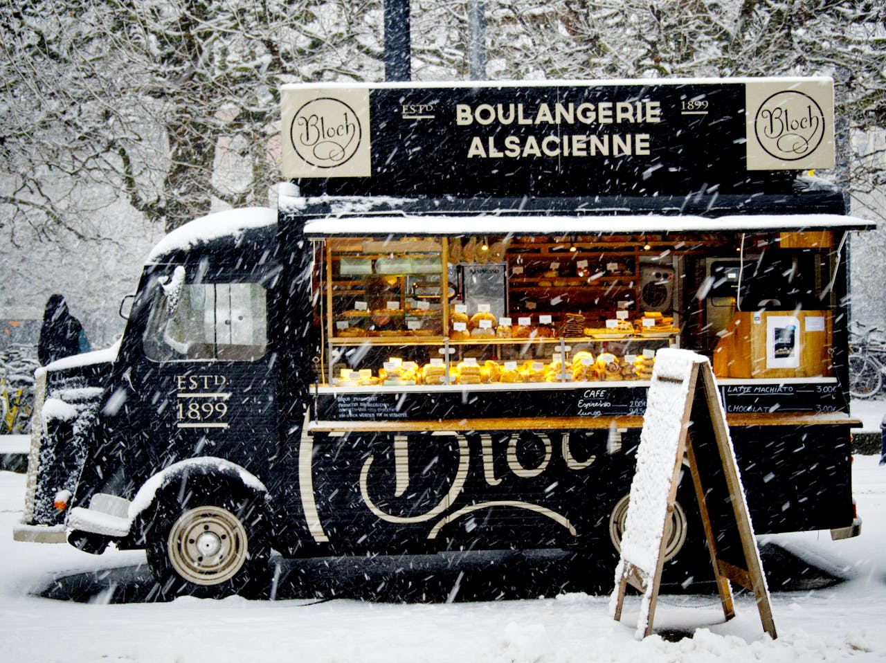 A vintage food truck in a snowy urban setting, offering baked goods and warmth during winter.